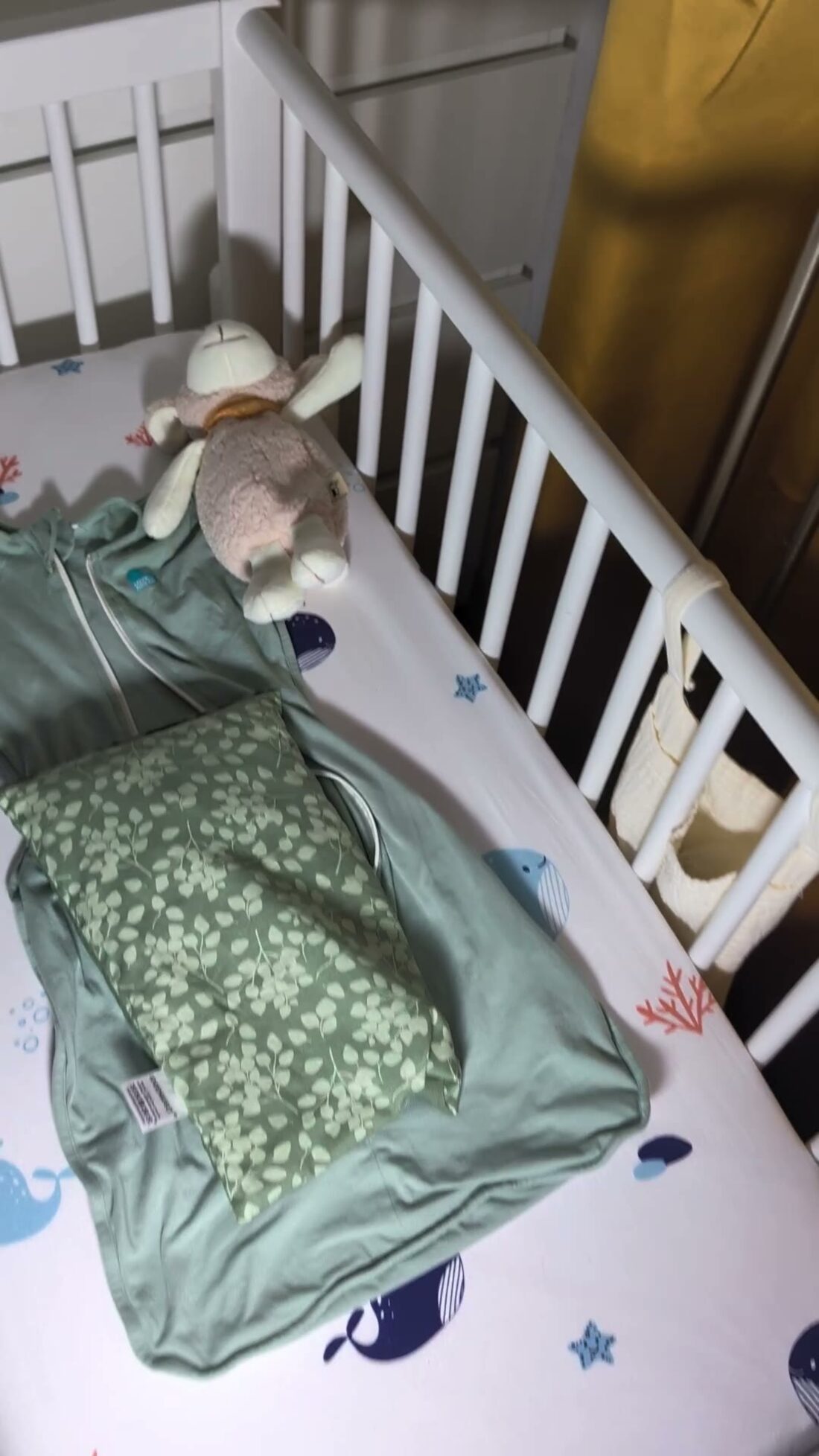 Ein Beistellbett mit grünem Schlafsack und einem Kuscheltier, von oben fotografiert.